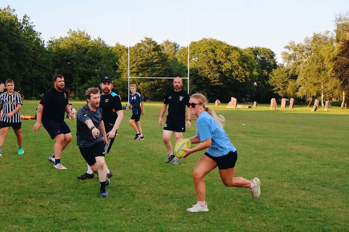 A coed touch rugby team tries stop a blonde player with the ball.