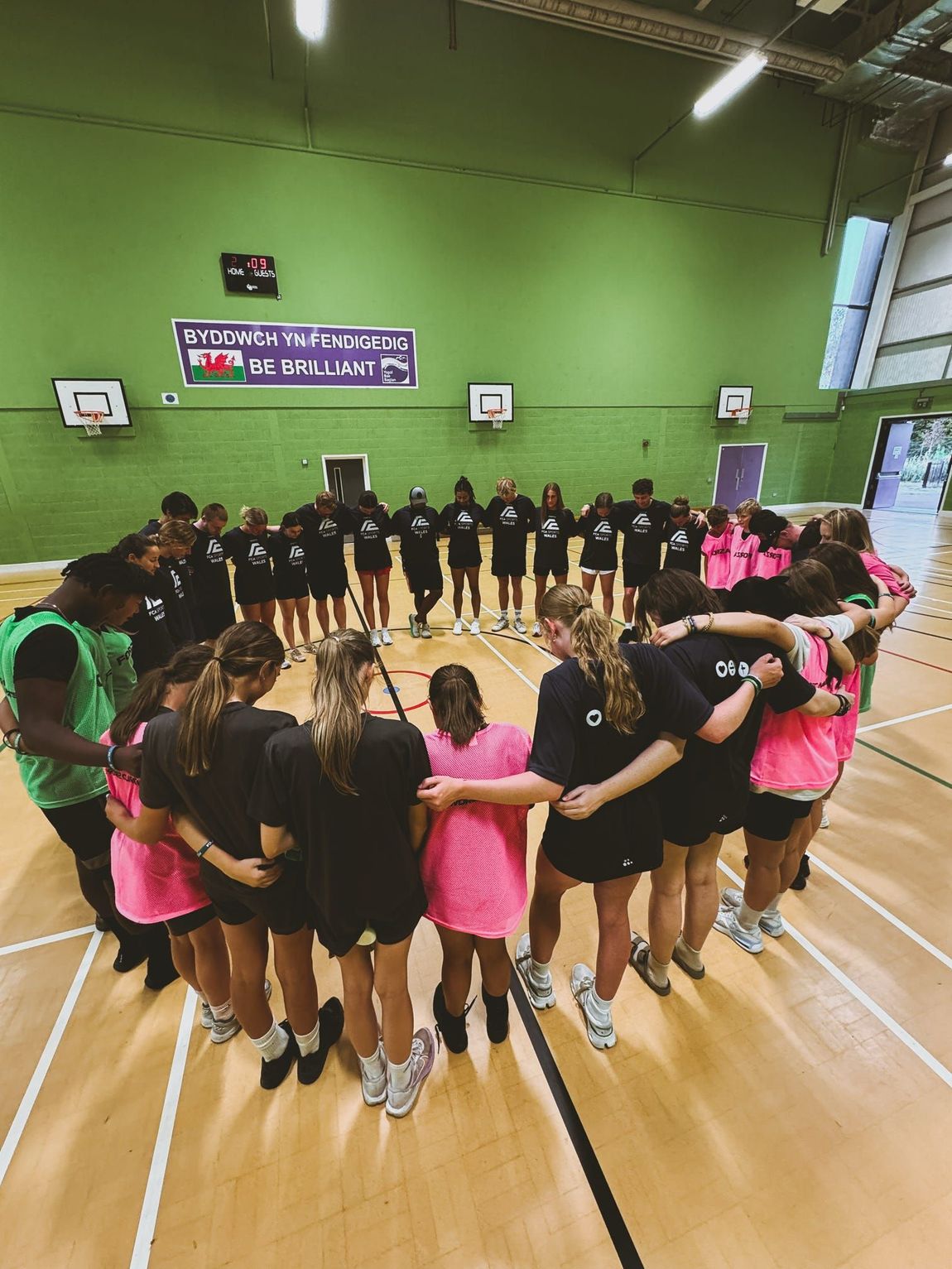 A group of athletes from different teams stands in a huddle praying.
