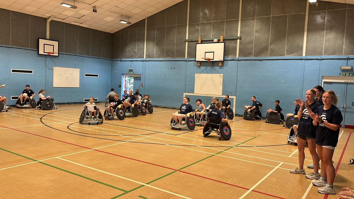 A group of children and adults play wheelchair rugby on a basketball court.