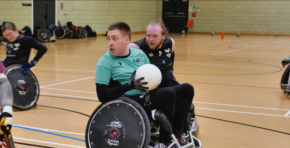 Two men on different teams play wheelchair rugby, one of them trying to steal the ball.