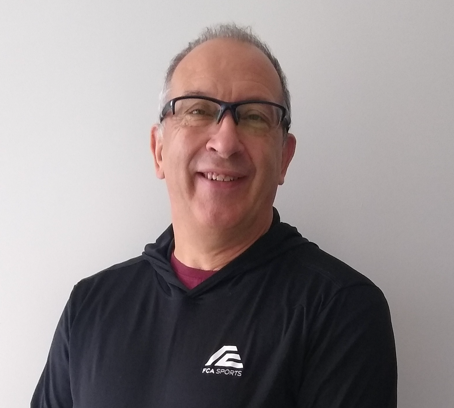 A white man in his sixties, grey hair and black-rimmed glasses, wearing a black FCA Sports shirt.