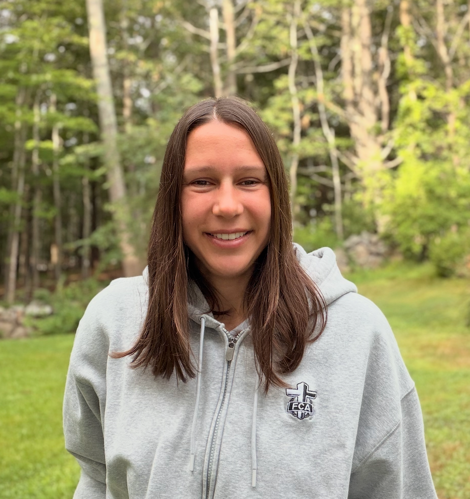 A woman in her twenties with long brown hair, wearing a grey FCA jumper.