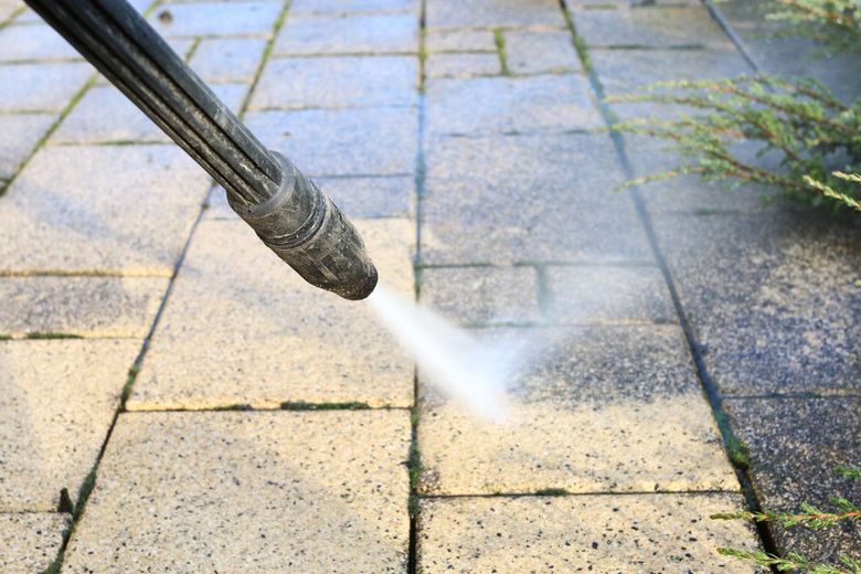 Pressure washer spraying water on dirty patio tiles outdoors