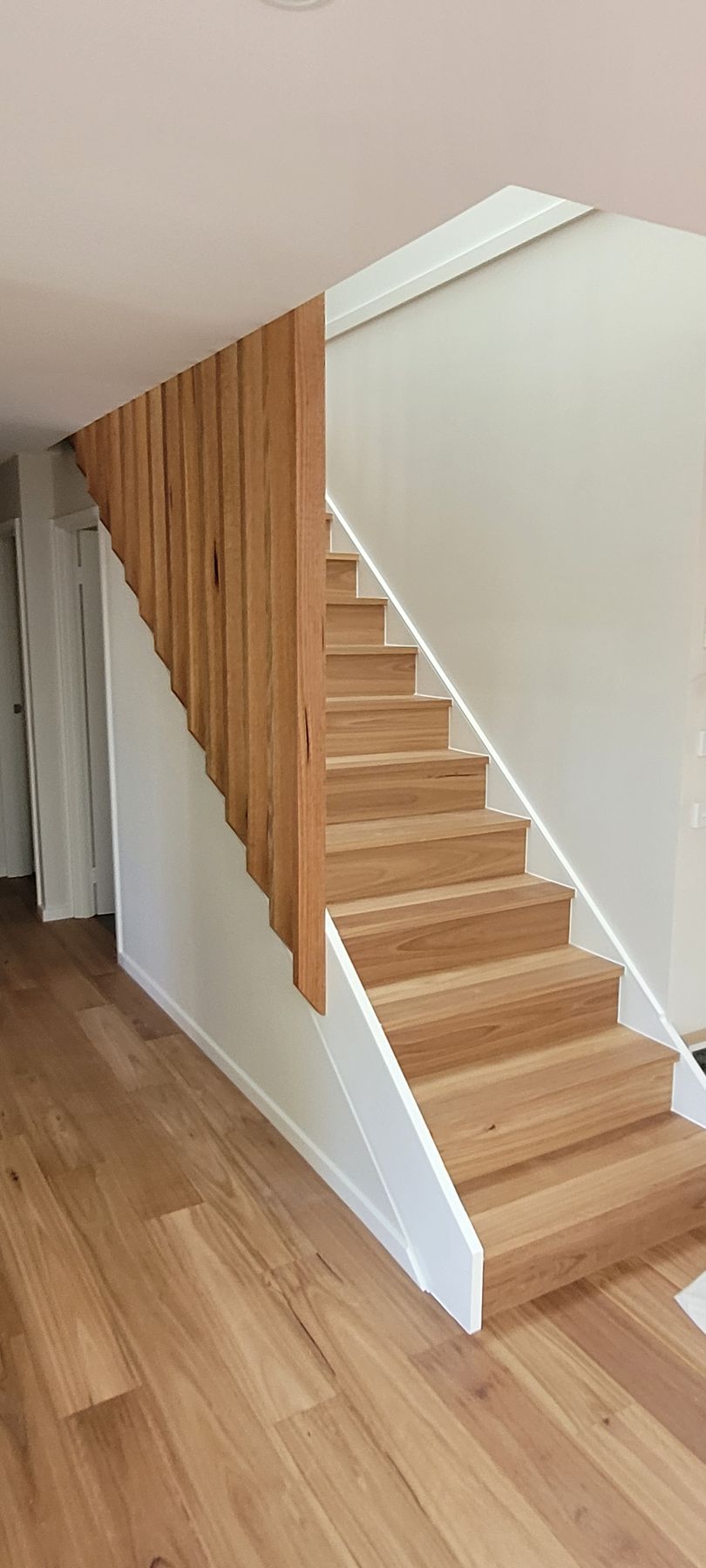 Wooden staircase with light wood steps and a vertical wood panel wall next to it.