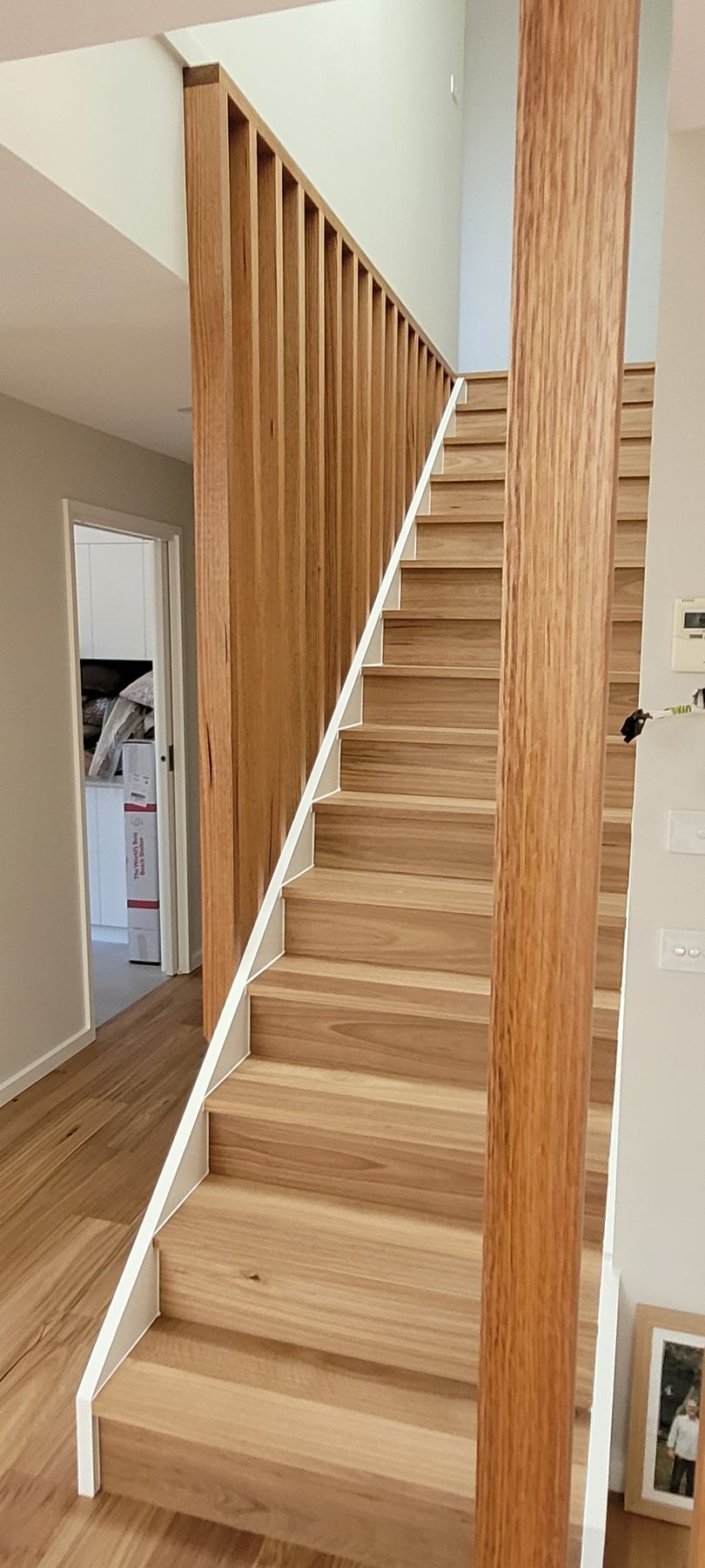 Wooden staircase with vertical railing leading upwards. Bright, natural light and wood tones.
