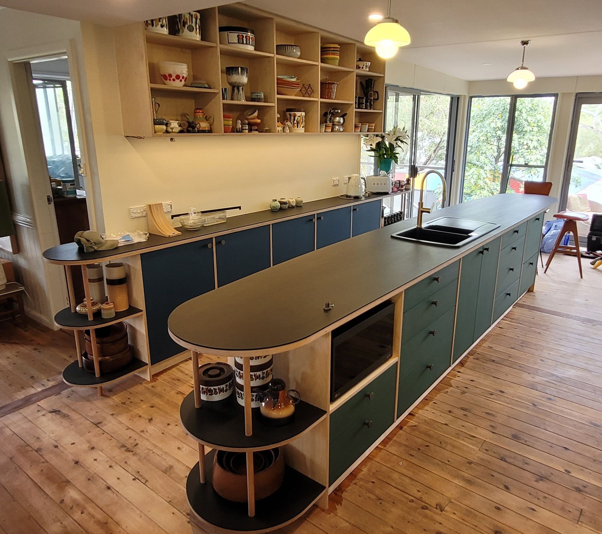 Modern kitchen with long, dark-topped island and light wood cabinets, shelving.