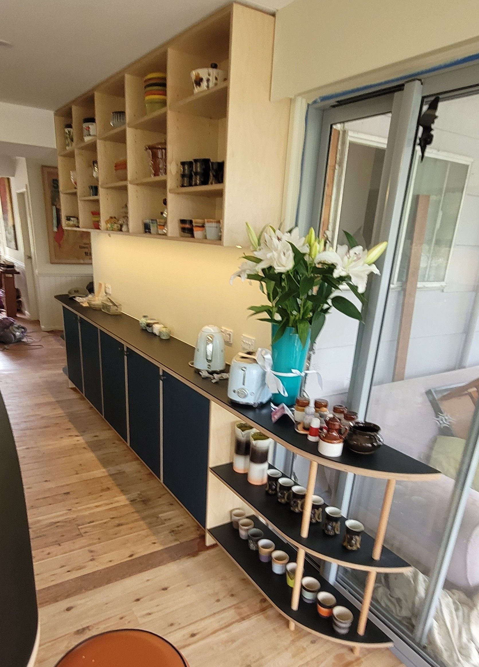 Hallway with wall shelves, dark cabinets, a glass shelf of candles, and a vase of white flowers by a window
