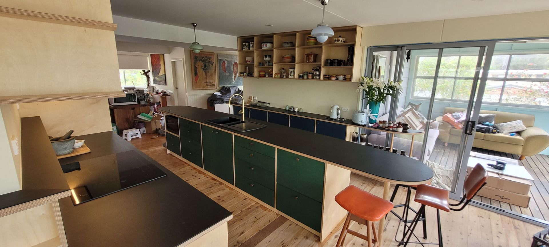 A retro kitchen with green cabinets, a dark countertop, and bar stools next to a sliding glass door.