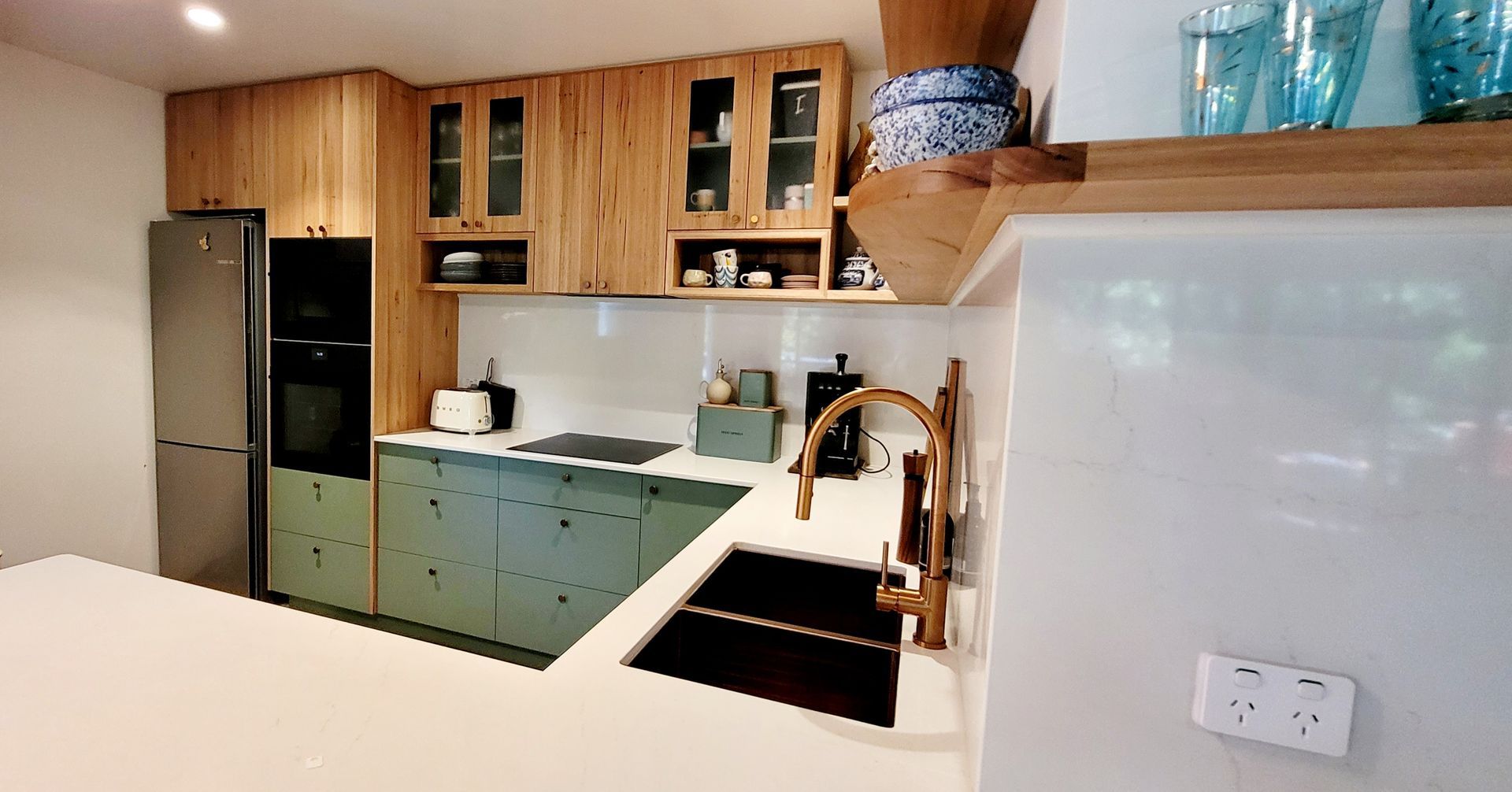 Modern kitchen with wood cabinets, teal lower cabinets, stainless fridge, and white countertop with sink.