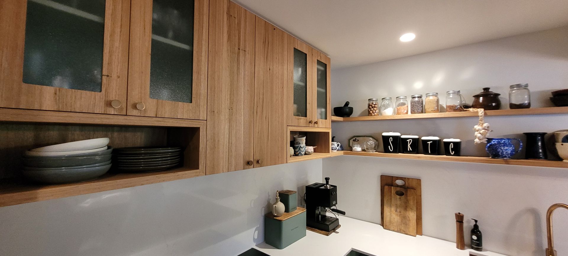 Wooden kitchen shelves with dishes, jars, and decor under warm under-cabinet lighting.