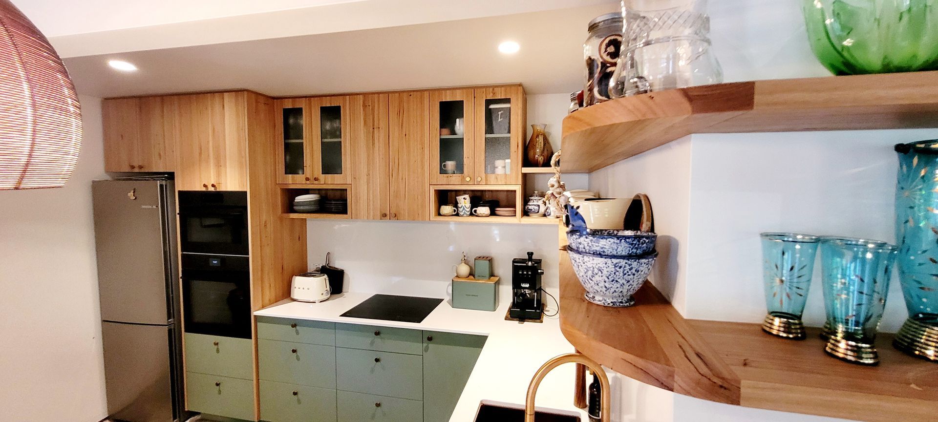 Modern kitchen with wood cabinets, stainless fridge, light countertops, and blue glass decor on shelves