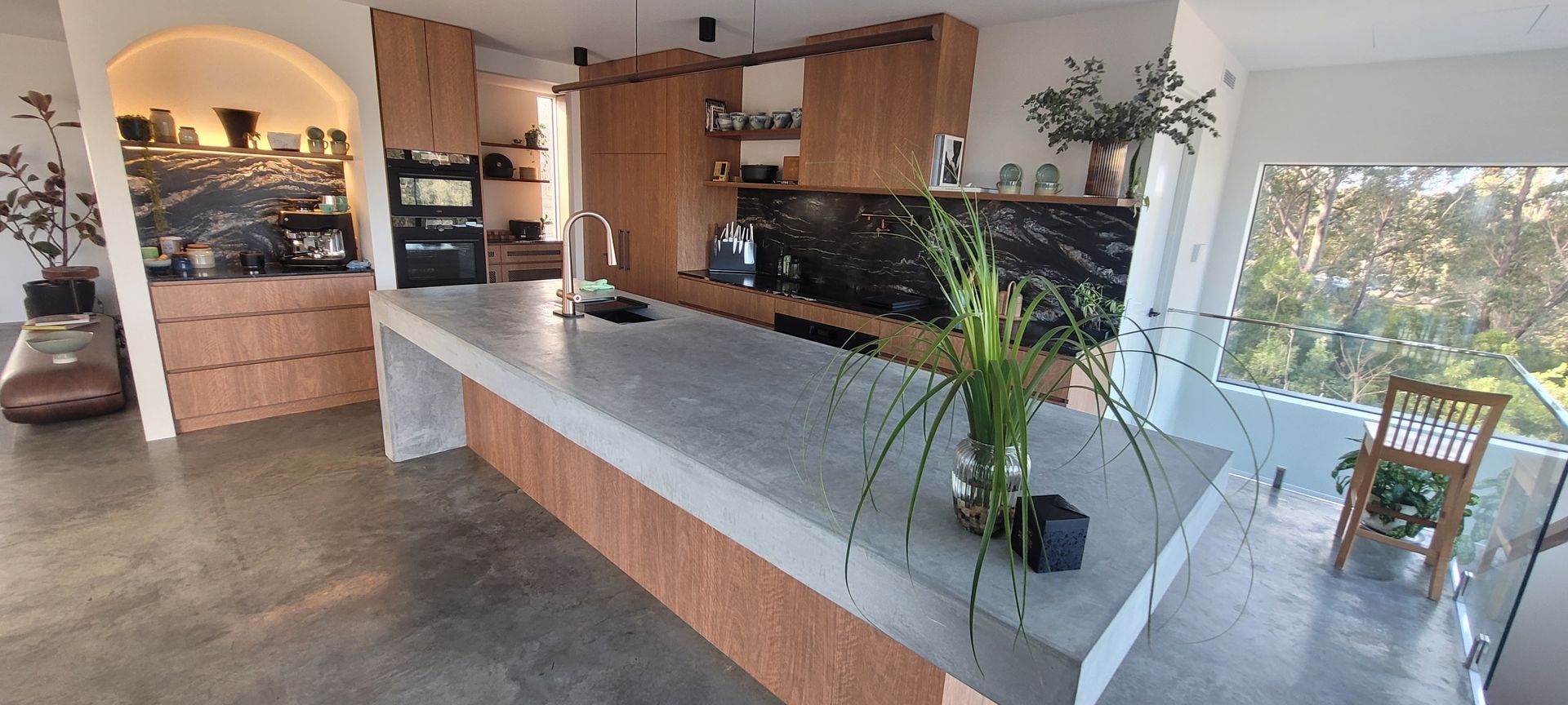 Bright modern kitchen with white island, wooden cabinets, large windows, and potted plants