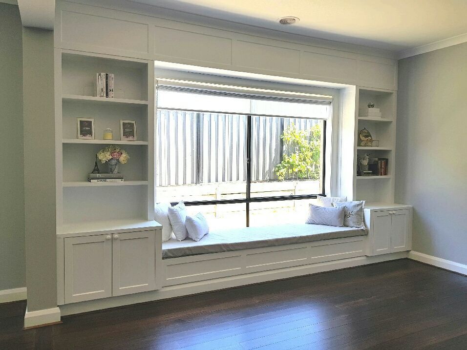 Built-in white window seat with bookshelves and cabinets, set against a window overlooking a fence.