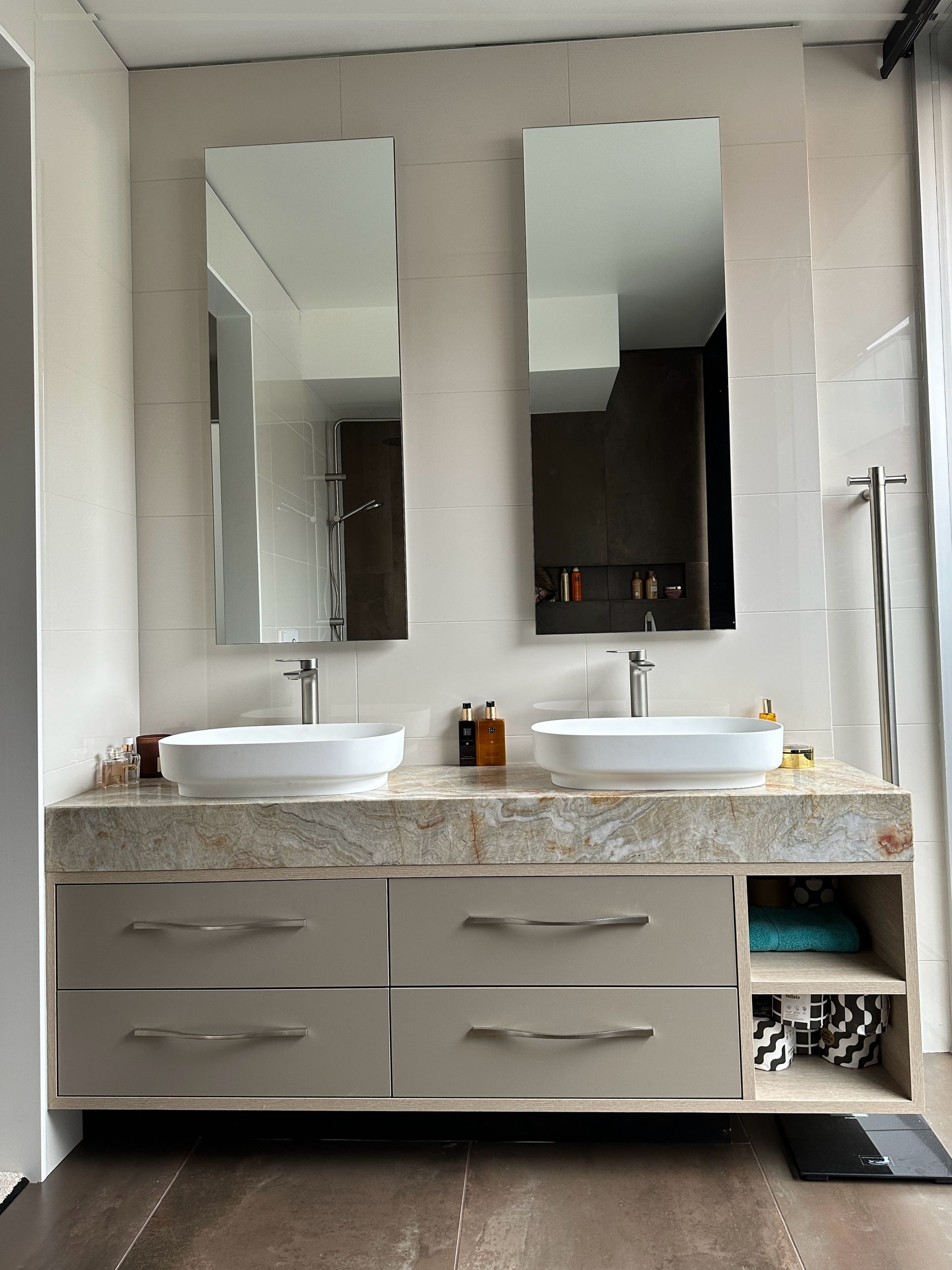 Modern bathroom with dual sinks, mirrors, and drawers. Neutral tones, stone countertop, and wood floors.