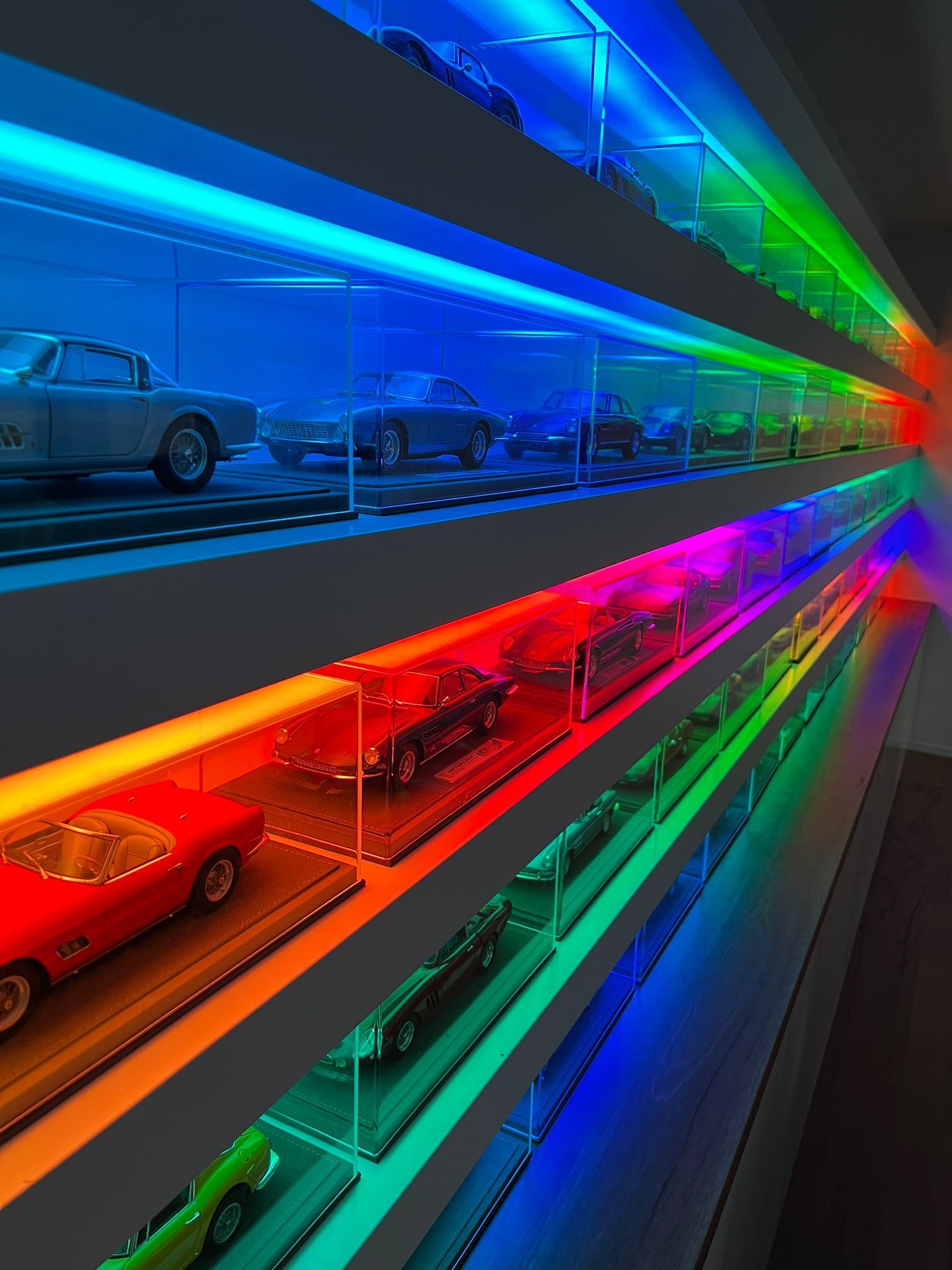 Display case with model cars, lit by vibrant rainbow LED lights.