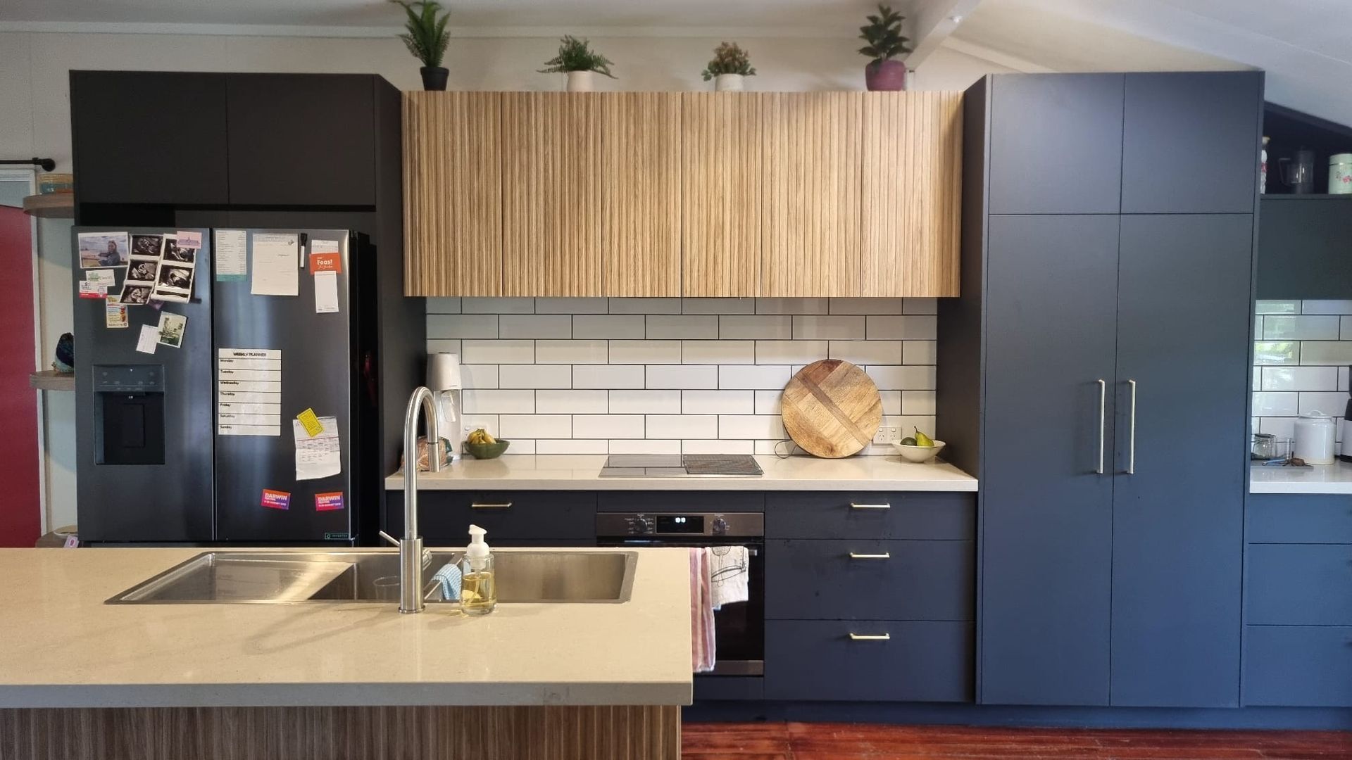 Modern kitchen with dark blue and wood cabinets, stainless steel appliances, and a light countertop.