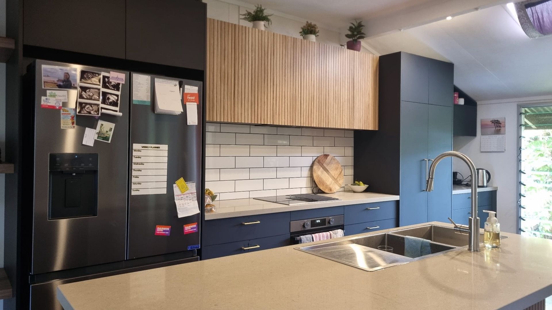 Modern kitchen with dark cabinetry, stainless steel fridge, and light wood accent cabinets above the sink.