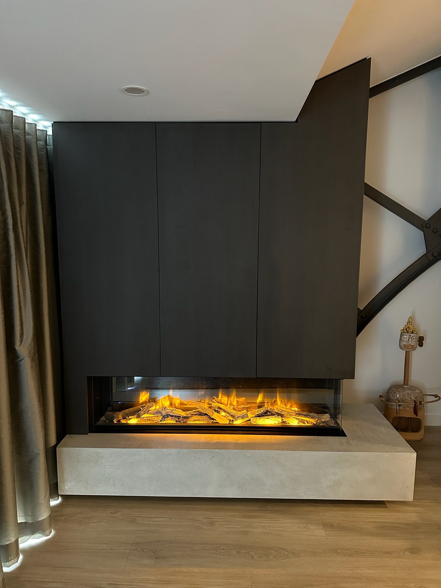 Modern fireplace with glowing flames, built into a dark gray wall, on a concrete hearth.