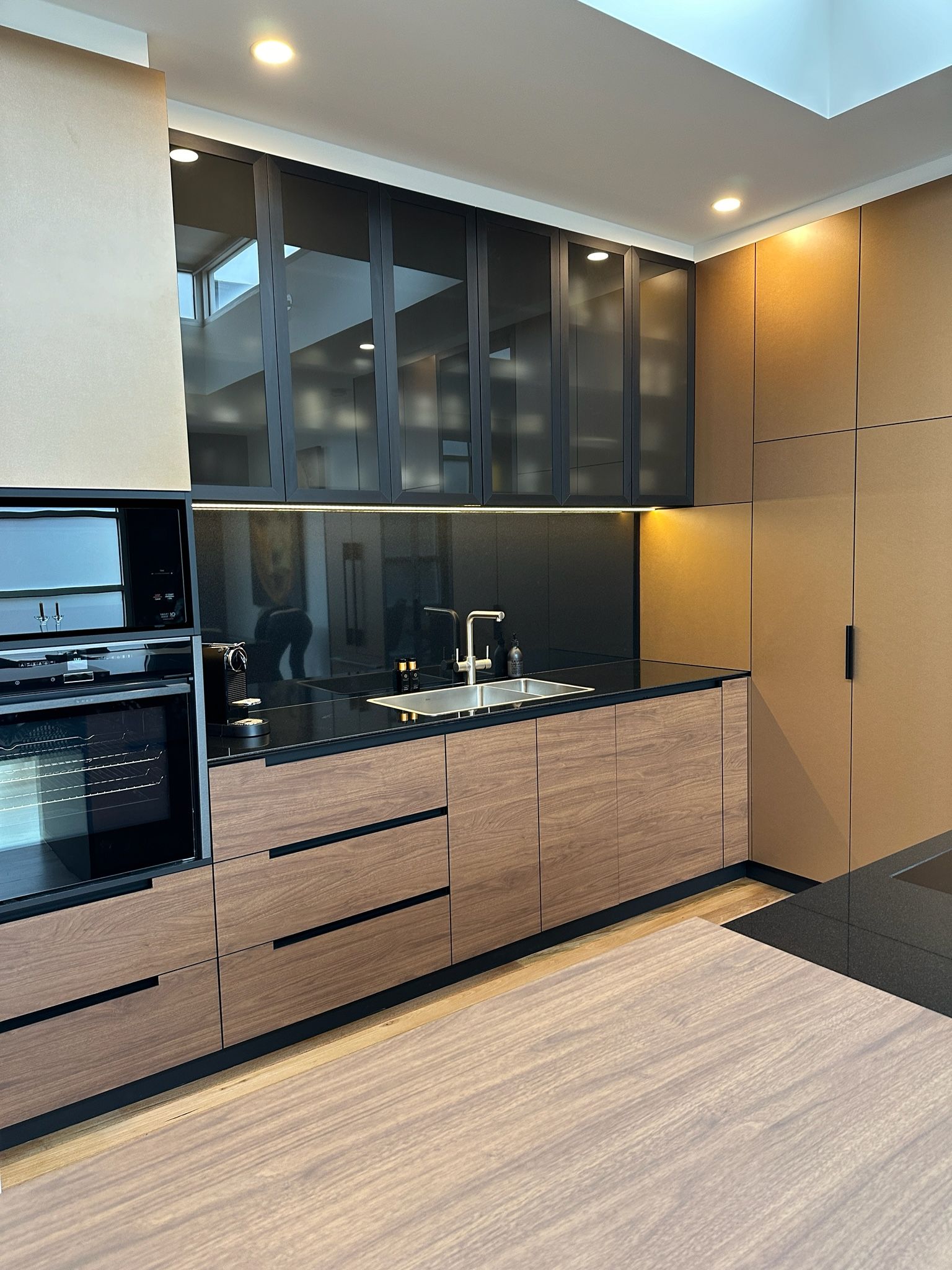 Modern kitchen with wood grain cabinets, black countertops and upper glass-front cabinets.