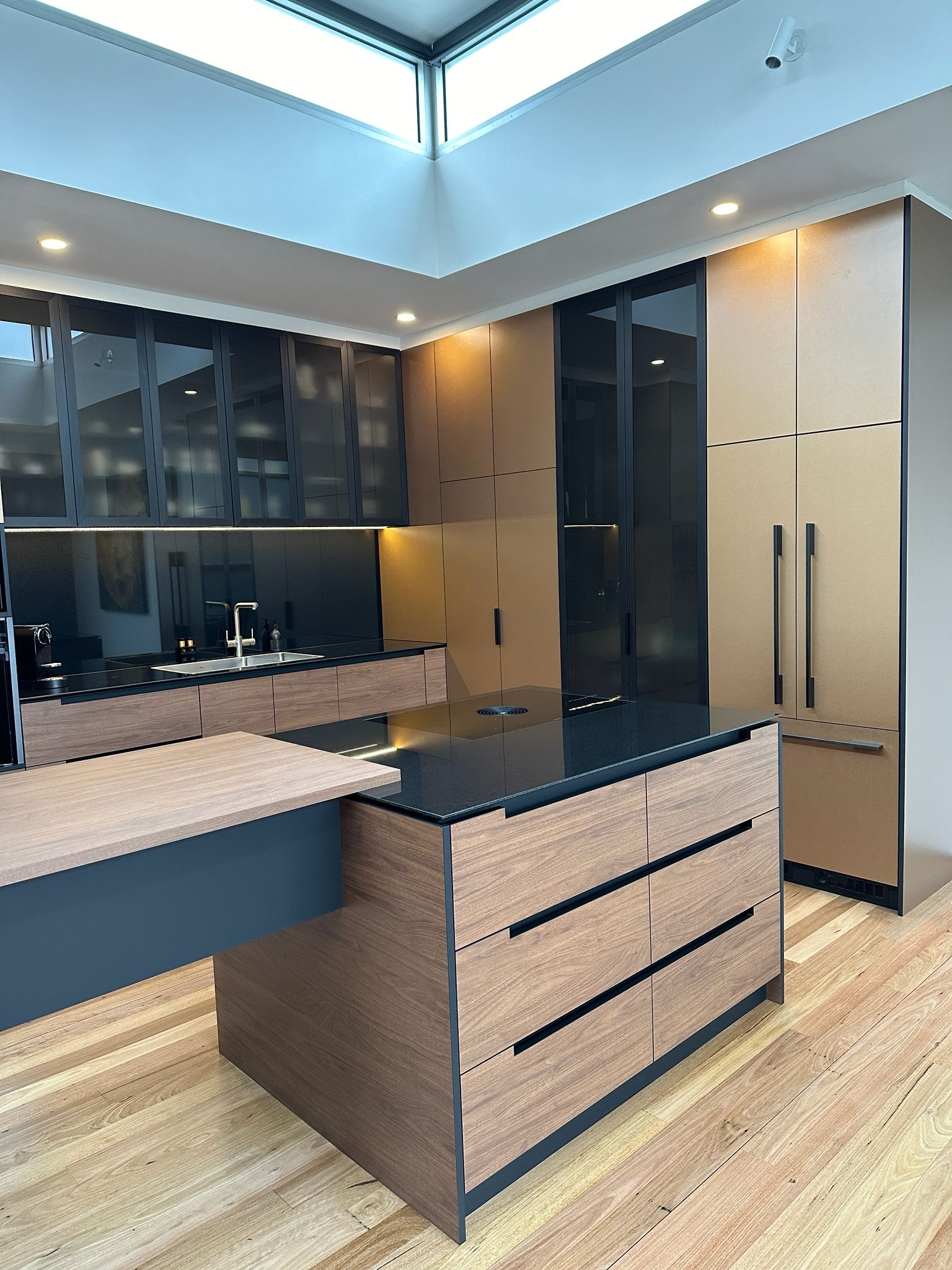 Modern kitchen with wood and black cabinetry, black island, light wood floor, and skylight.