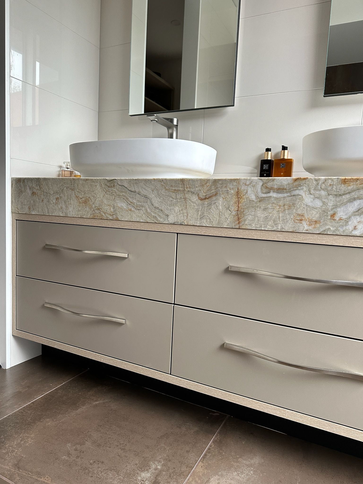 Bathroom vanity with light gray drawers, stone countertop, white sinks, and mirrors.