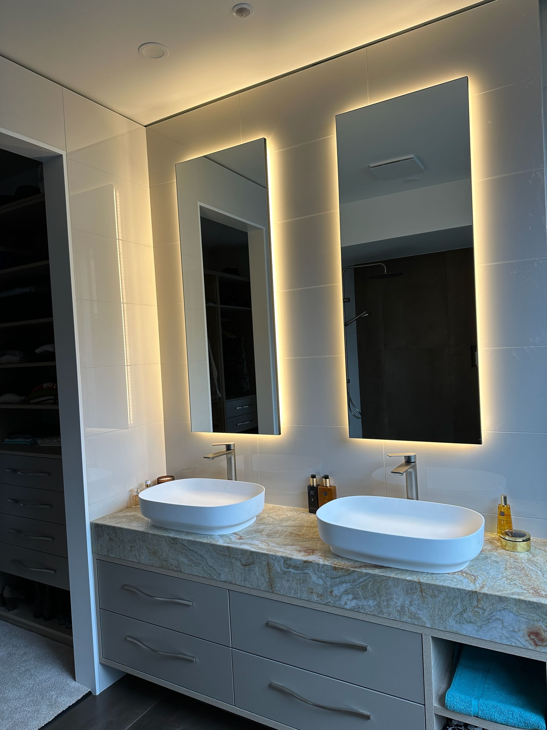 Modern bathroom with two illuminated mirrors above sinks on a gray marble countertop.