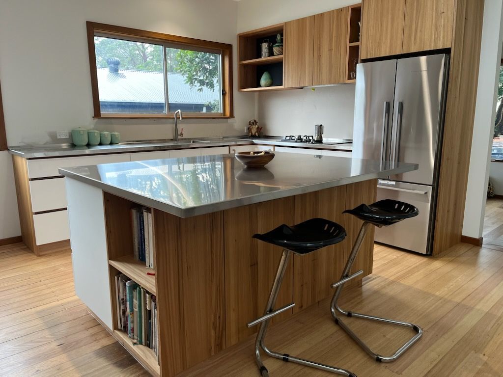 Modern kitchen with wooden cabinets, island, and stainless steel refrigerator. Two bar stools are at the island.
