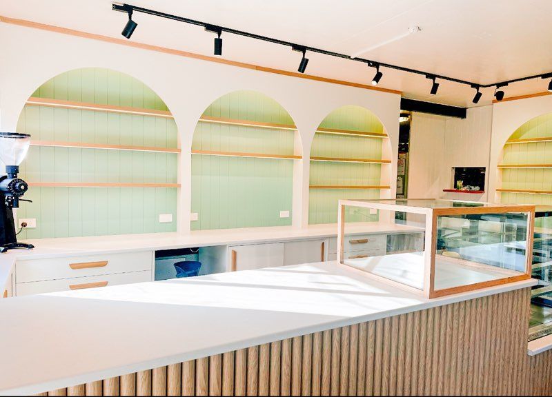 Interior of a bright cafe with white counters, wooden shelves, and a display case.