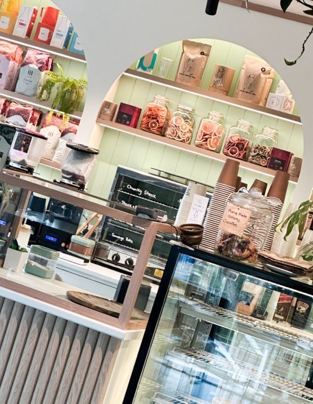 Interior of a cafe with a counter, baked goods, shelves of jars, and coffee machines.