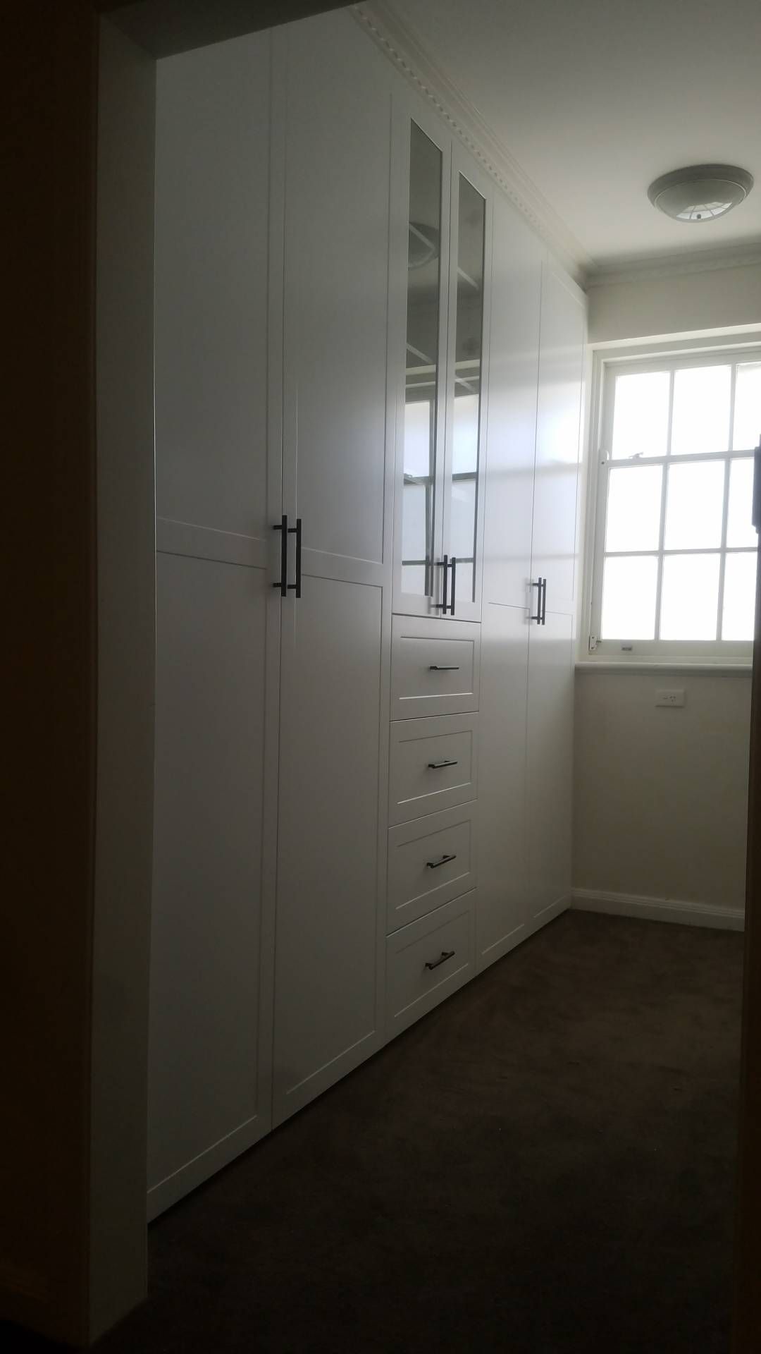 White built-in closet with black handles. A window is in the background. Brown carpet.