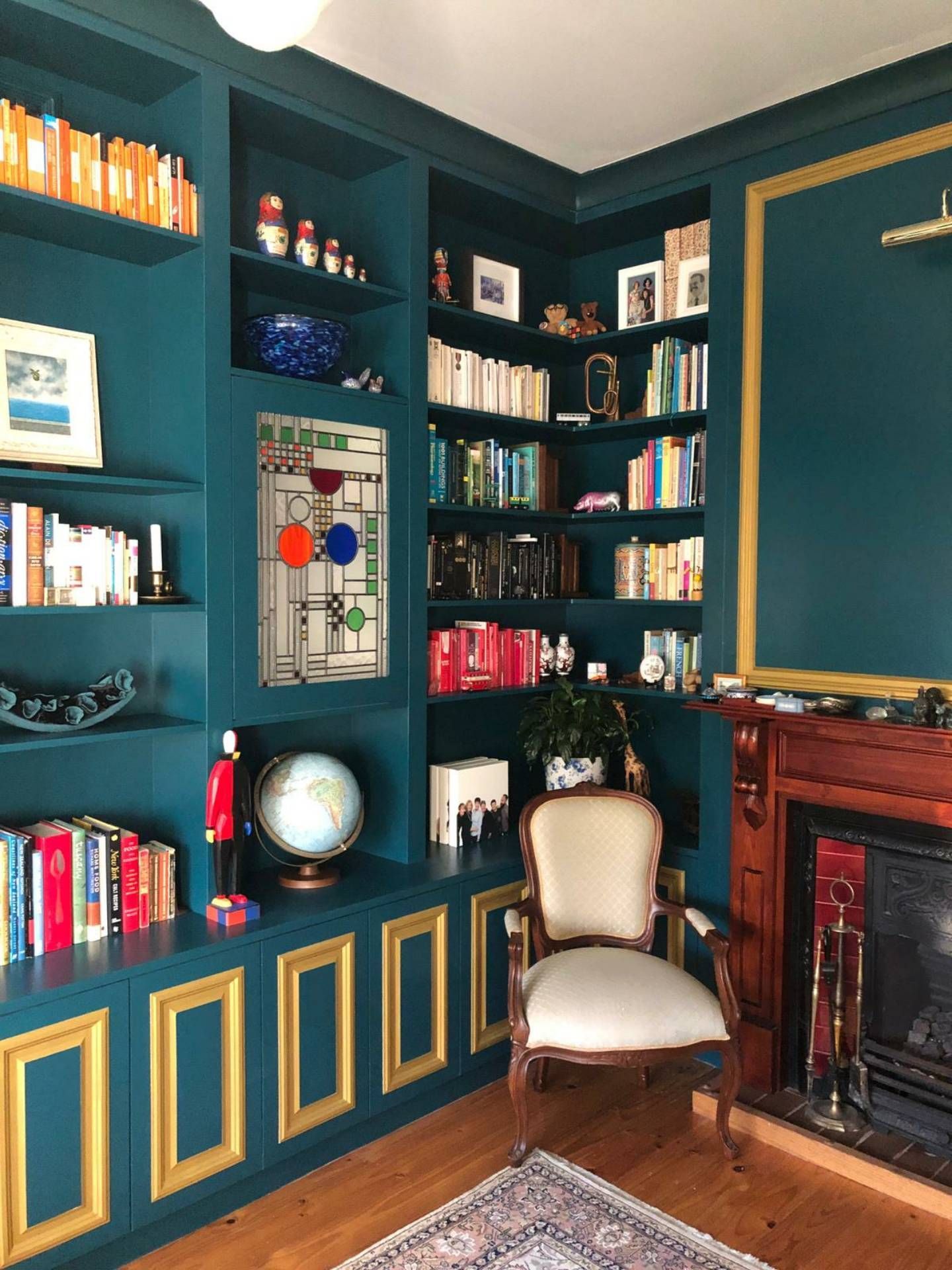 Teal built-in bookshelves and fireplace with gold trim, filled with books, decor, and a white chair.