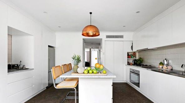 Modern white kitchen with island, copper pendant light, and dark wood floor.