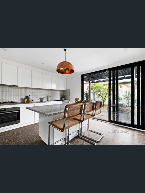 Modern white kitchen with a granite island, copper pendant light, and sliding doors to an outdoor area.