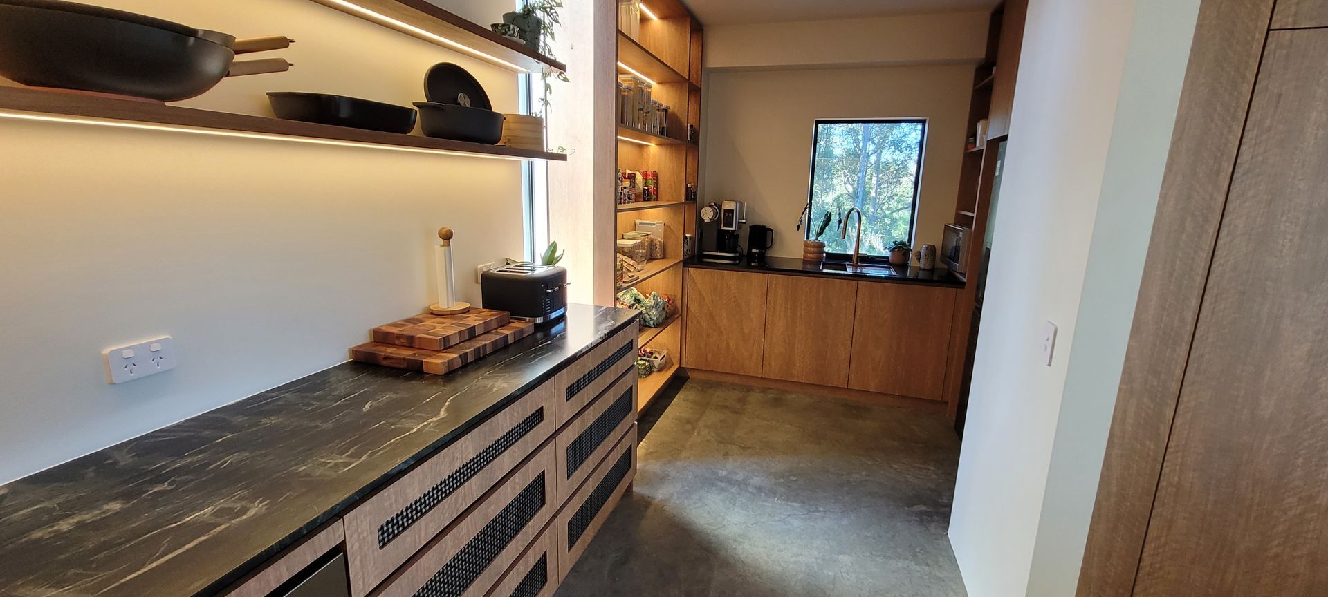 Modern kitchen hallway with wood cabinets, gray tile floor, and black countertop decor