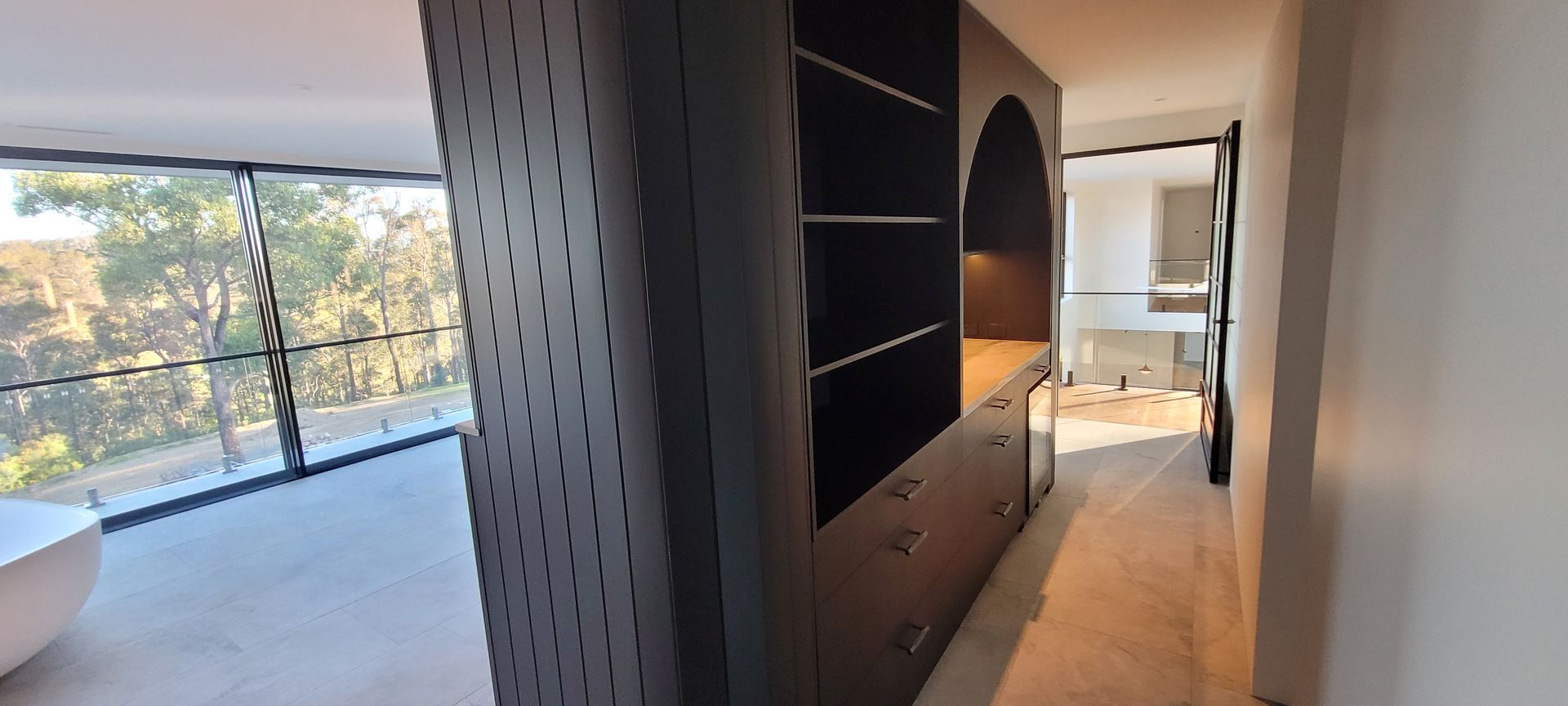 Modern hallway with built-in shelves, leading to a bright balcony and bathroom