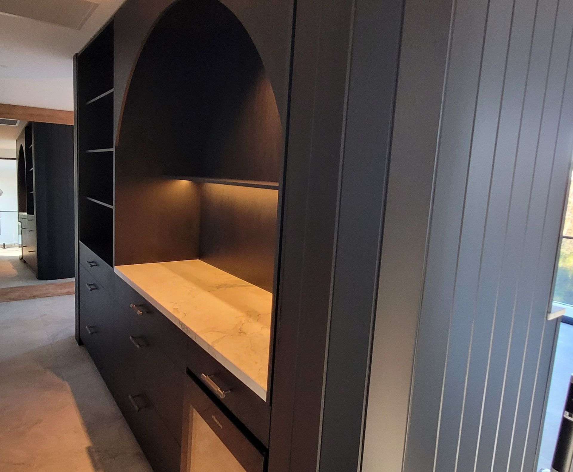 Built-in dark wood shelving nook with warm underlighting and drawers in a hallway