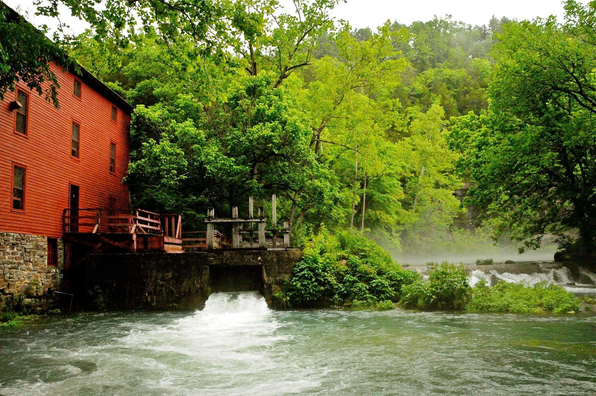 Ozark National Scenic Riverways. Red mill by a rushing river, surrounded by green trees.