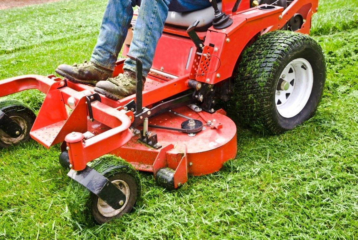 Person operating a red riding lawn mower on green grass