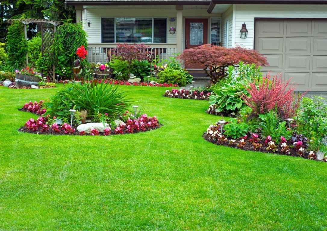 Front yard garden with colorful flower beds and a green lawn beside a house and garage