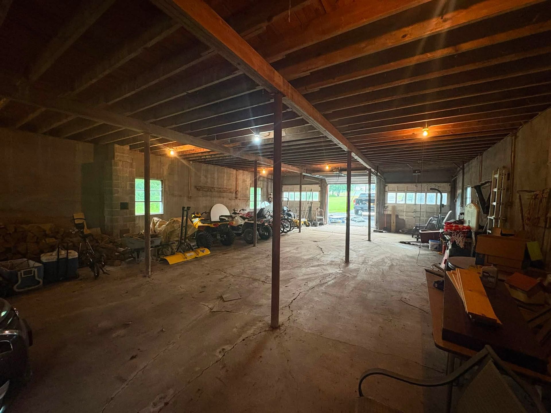 Empty unfinished warehouse with exposed beams, concrete floor, and tools and equipment along the sides.