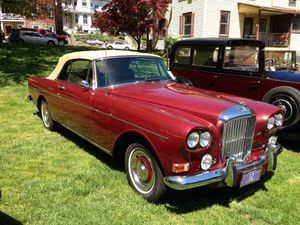 A red car with a white top is parked in the grass.
