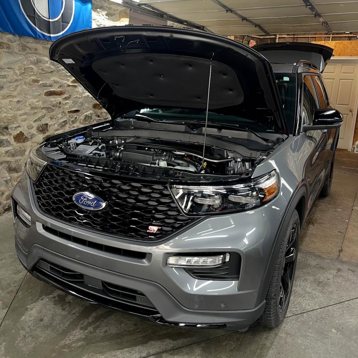 A gray ford suv with the hood up is parked in a garage.