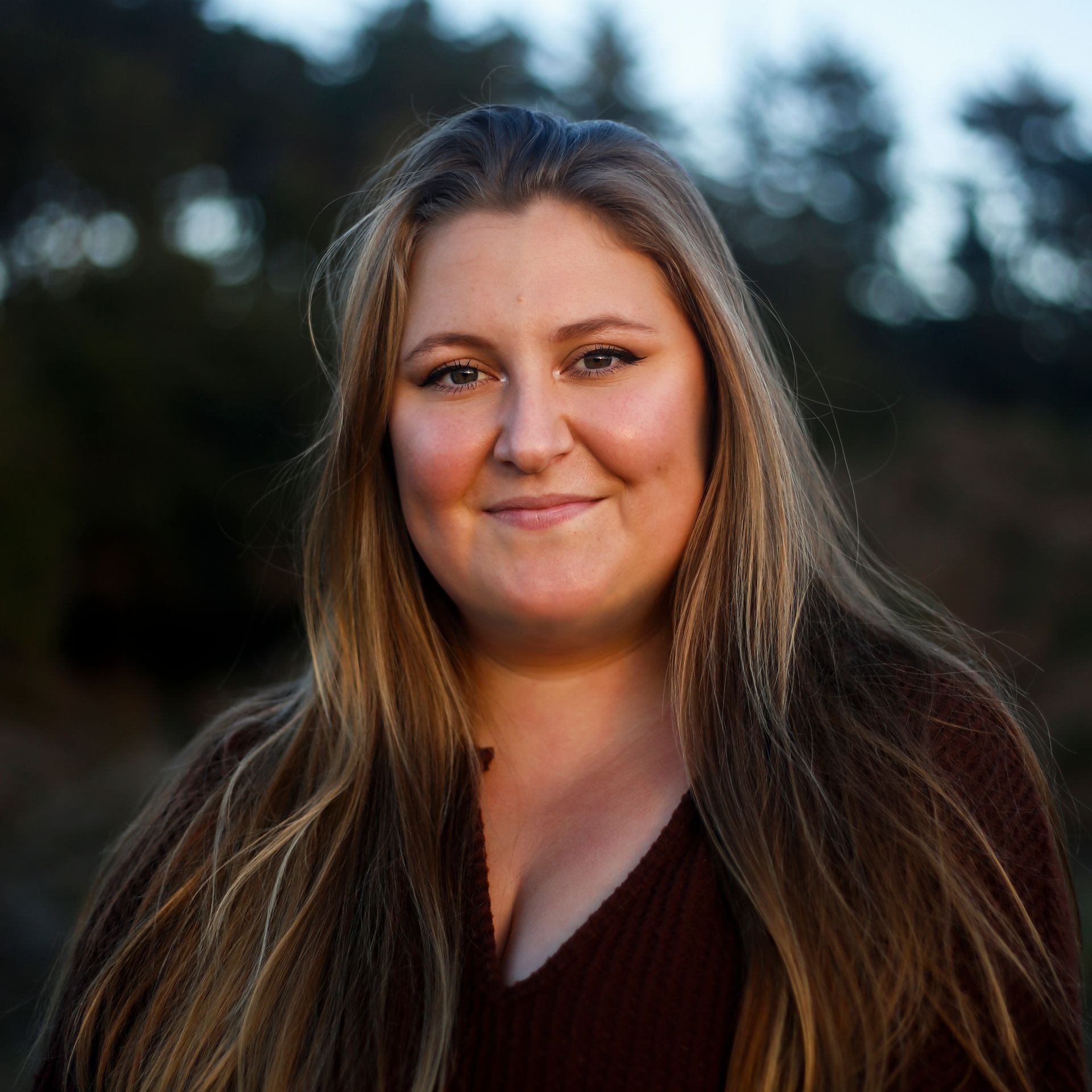 A woman (Delaney Mayo) with long hair is smiling for the camera