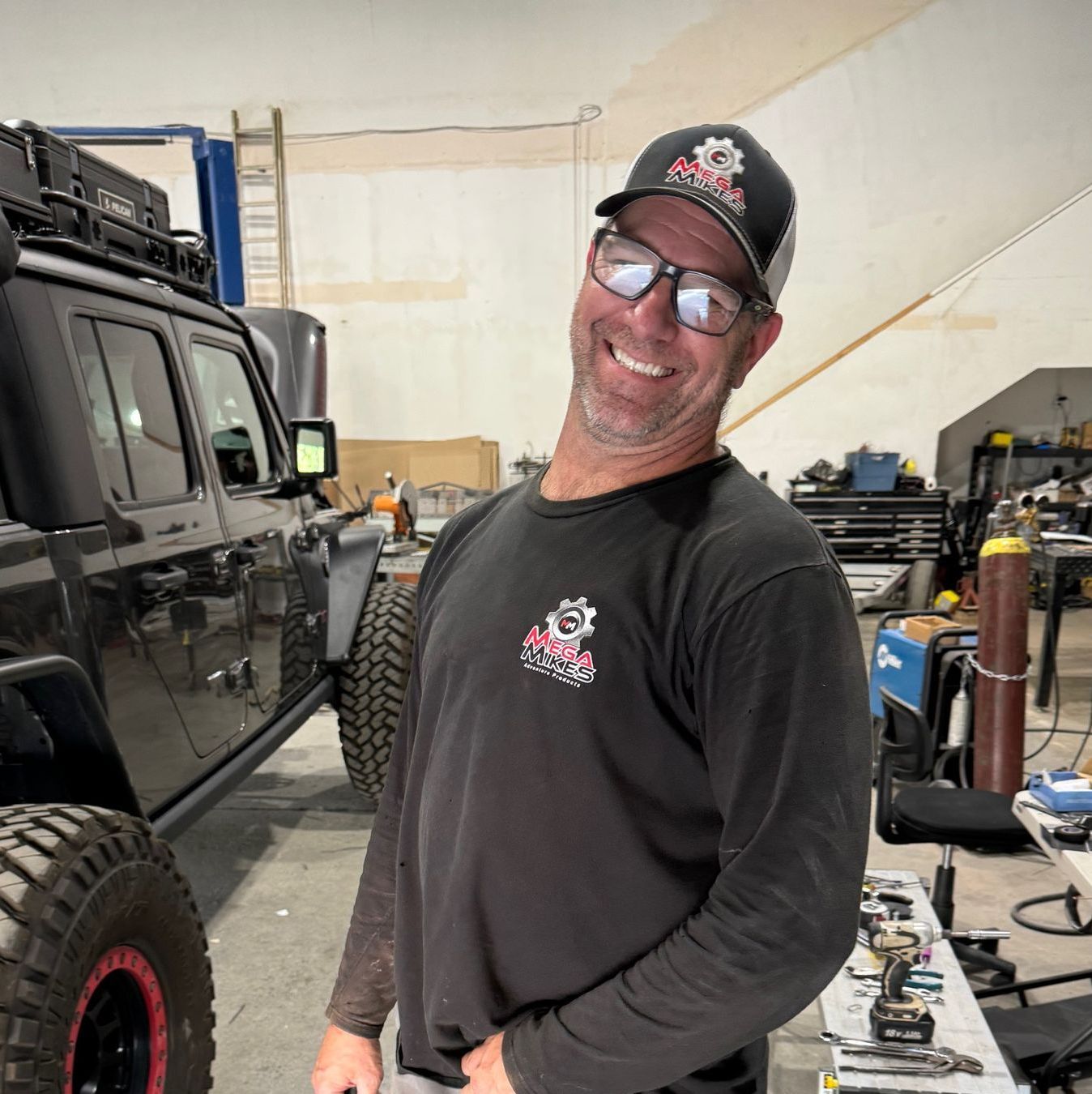 A man Mike Hodkin is standing in front of a jeep in a garage.