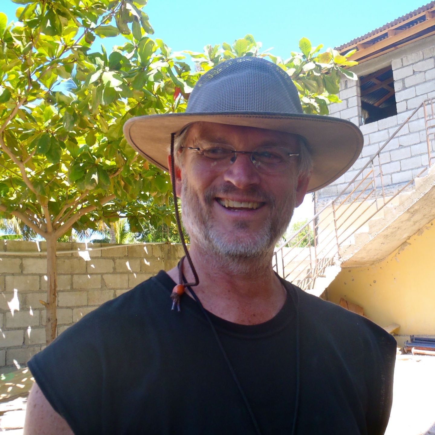 Steve Collom wearing a hat and glasses smiles for the camera