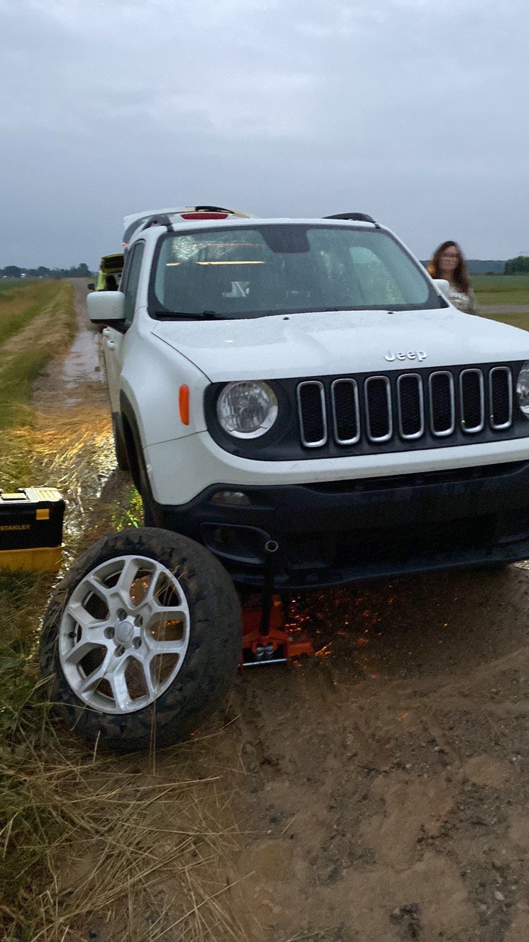 A white jeep renegade is sitting on the side of a dirt road with a flat tire.