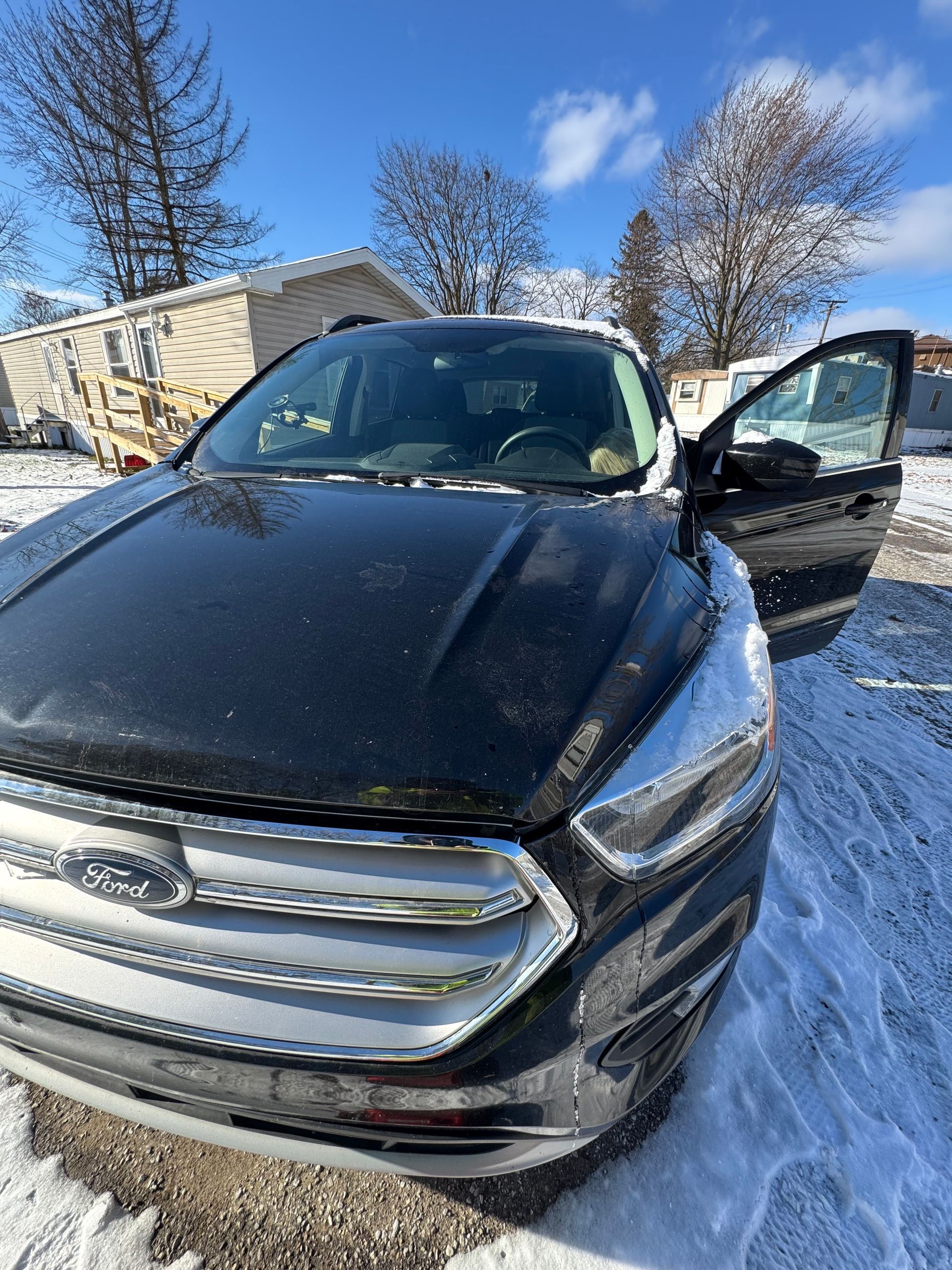 A black ford escape is parked in the snow with its doors open.