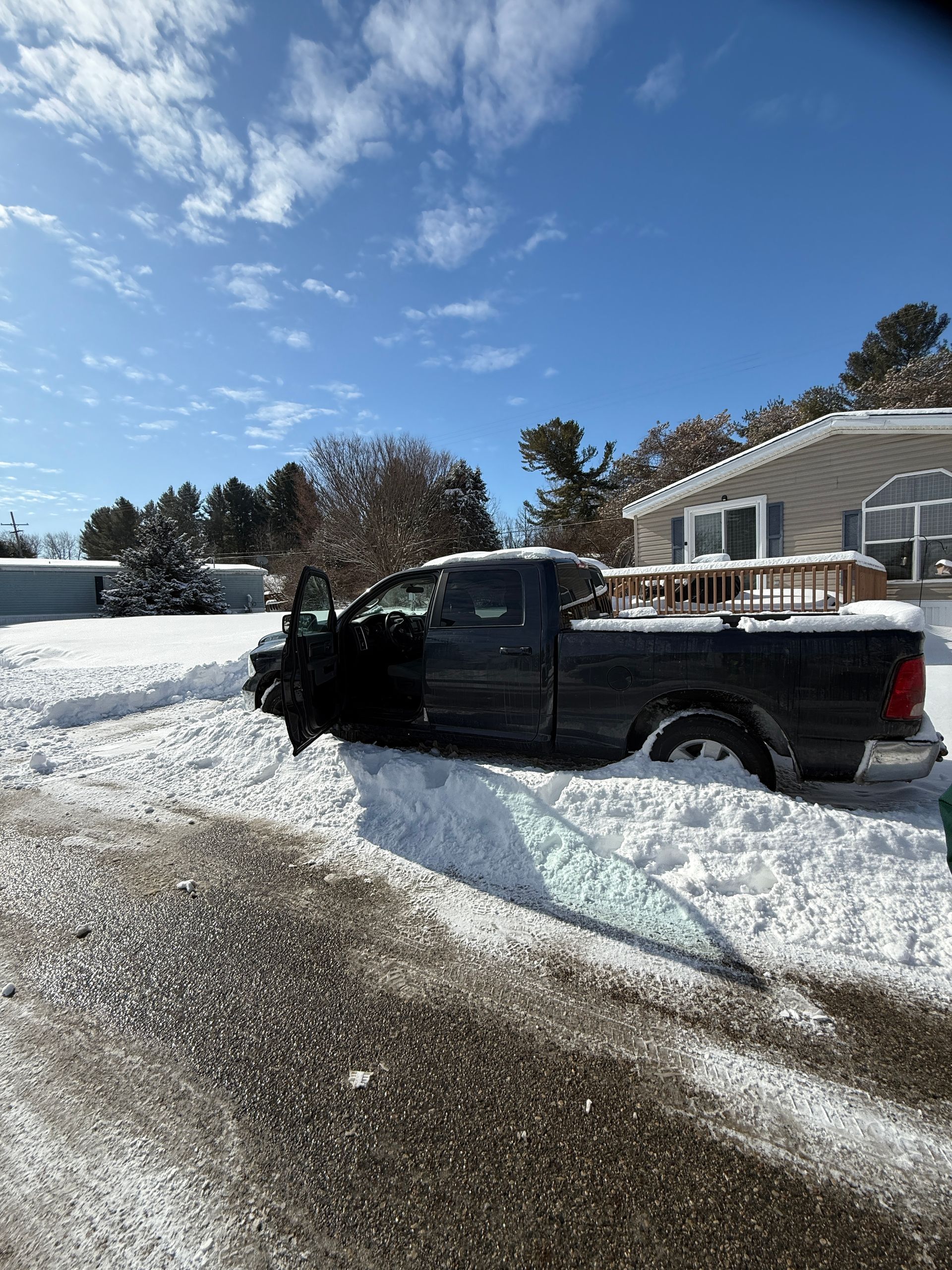 A black truck is parked in the snow in front of a house.