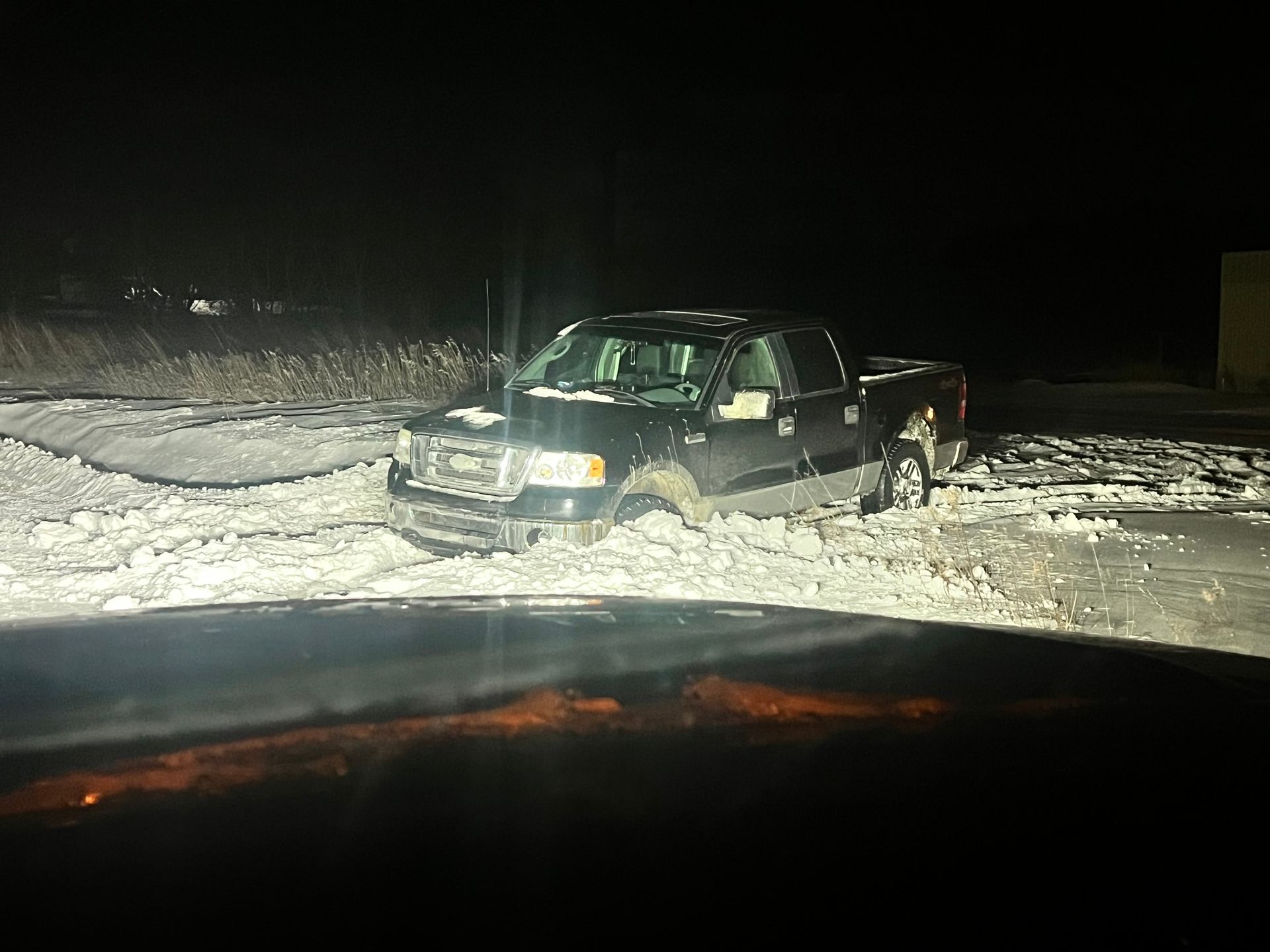 A black truck is stuck in the snow at night