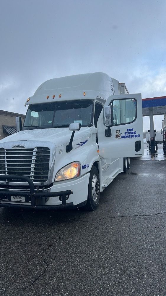 A white semi truck is parked in front of a gas station with its doors open.